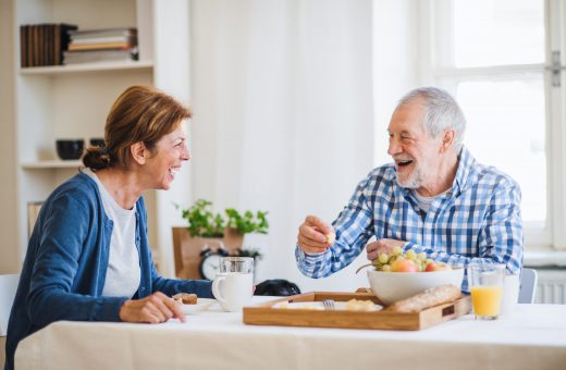 A happy senior couple sitting at the table at home, having breakfast.